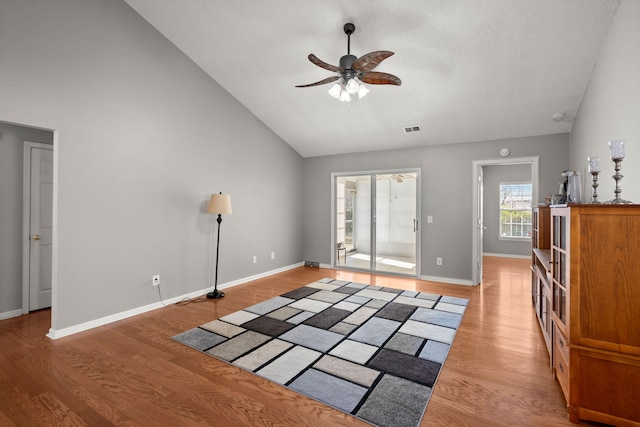 living area with light wood finished floors, visible vents, baseboards, ceiling fan, and high vaulted ceiling