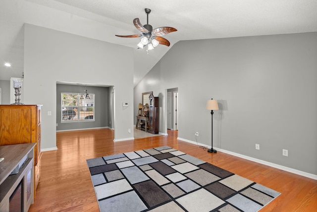 unfurnished living room with high vaulted ceiling, light wood-style flooring, baseboards, and ceiling fan with notable chandelier