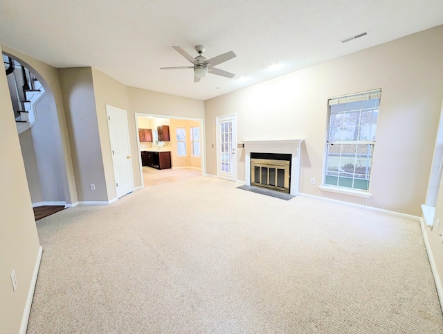 unfurnished living room featuring a healthy amount of sunlight, light colored carpet, and ceiling fan