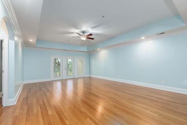 empty room with a raised ceiling, light hardwood / wood-style flooring, french doors, and ornamental molding