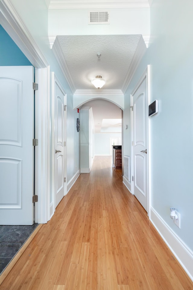 hallway featuring light hardwood / wood-style floors, ornamental molding, and a textured ceiling