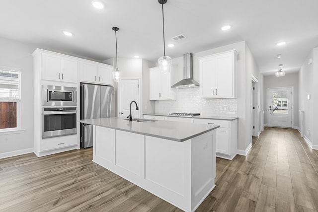 kitchen with visible vents, a sink, stainless steel appliances, light wood-style floors, and wall chimney range hood