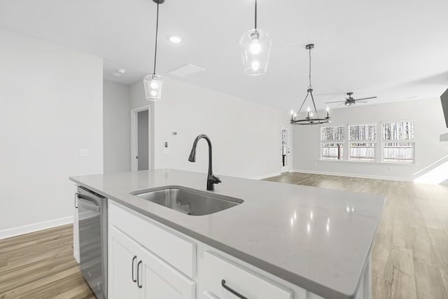 kitchen featuring light wood finished floors, a sink, decorative light fixtures, stainless steel dishwasher, and a kitchen island with sink