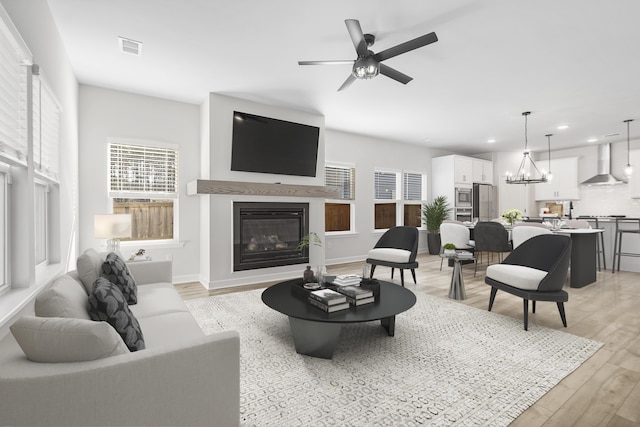 living area featuring visible vents, recessed lighting, light wood-style floors, a glass covered fireplace, and ceiling fan with notable chandelier