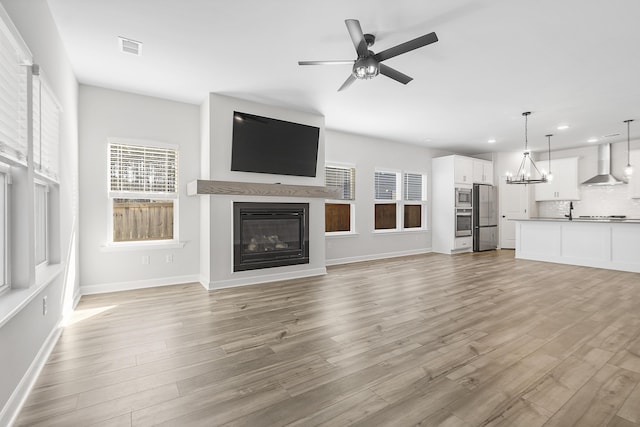 unfurnished living room featuring a glass covered fireplace, ceiling fan with notable chandelier, visible vents, and light wood-style floors