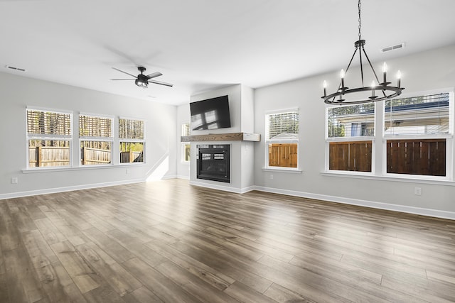 unfurnished living room featuring visible vents, a glass covered fireplace, dark wood finished floors, and ceiling fan with notable chandelier