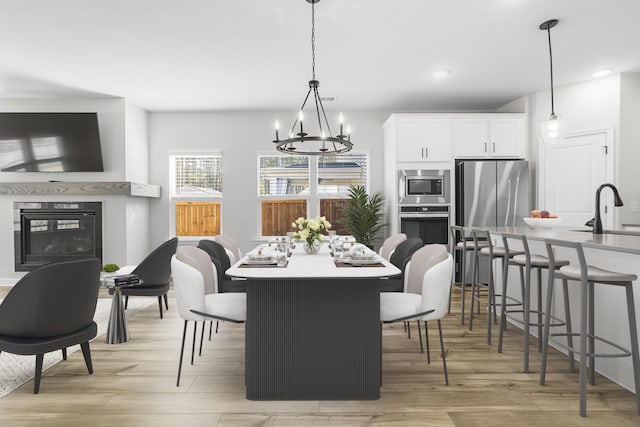 dining space featuring a notable chandelier, a glass covered fireplace, recessed lighting, and light wood-type flooring