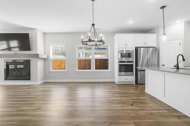 kitchen featuring white cabinetry, dark wood-style flooring, a sink, appliances with stainless steel finishes, and a glass covered fireplace