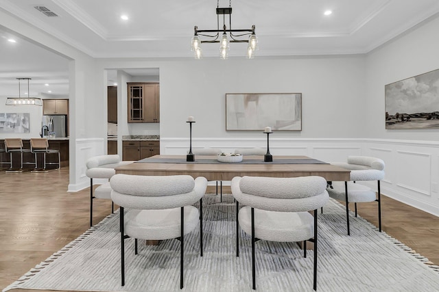 dining space with crown molding, a raised ceiling, light hardwood / wood-style flooring, and a notable chandelier