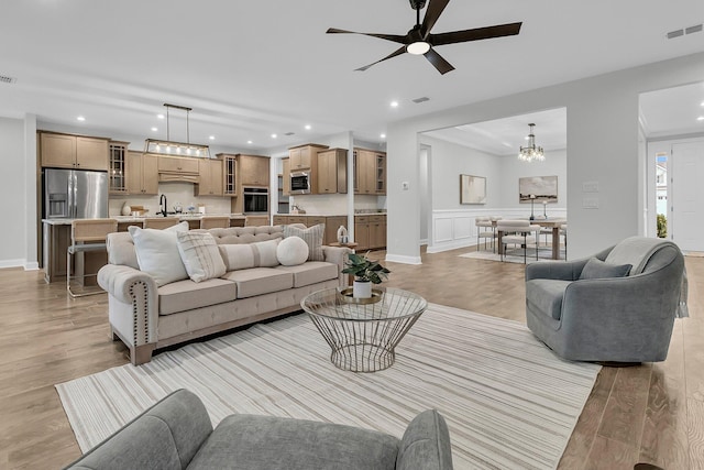 living room with sink, ceiling fan with notable chandelier, and light hardwood / wood-style floors