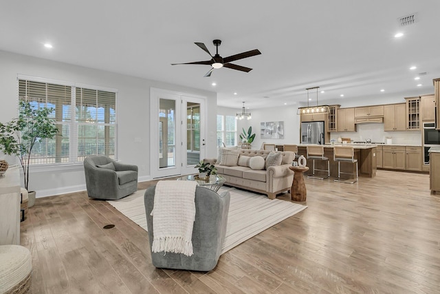 living room with ceiling fan with notable chandelier, light hardwood / wood-style floors, and a healthy amount of sunlight