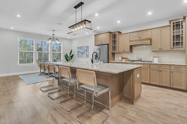 kitchen with decorative light fixtures, a kitchen bar, a large island with sink, stainless steel appliances, and light hardwood / wood-style flooring