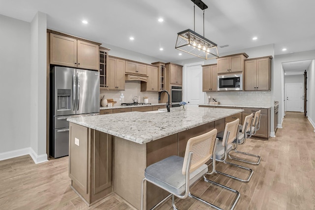 kitchen featuring a breakfast bar, light stone counters, a large island with sink, pendant lighting, and stainless steel appliances