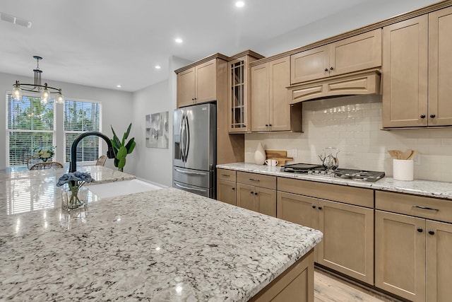 kitchen with appliances with stainless steel finishes, decorative light fixtures, sink, backsplash, and light stone counters