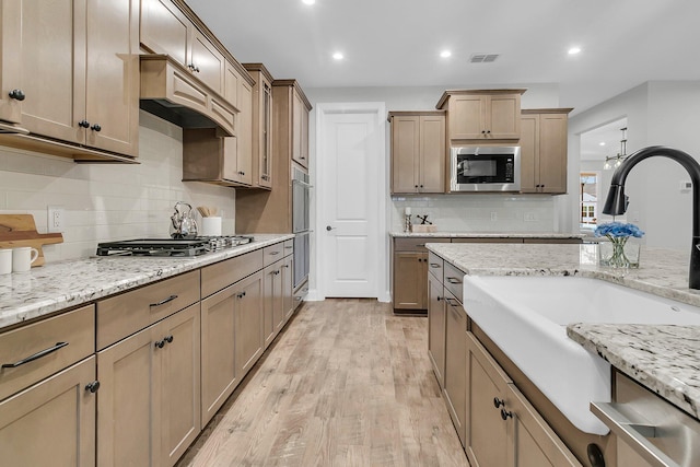 kitchen with sink, light wood-type flooring, appliances with stainless steel finishes, custom range hood, and light stone countertops