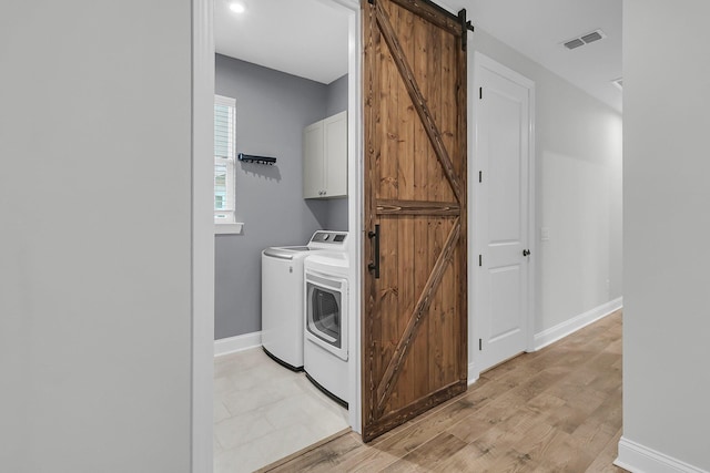 laundry room featuring cabinets, a barn door, light hardwood / wood-style floors, and washer and dryer