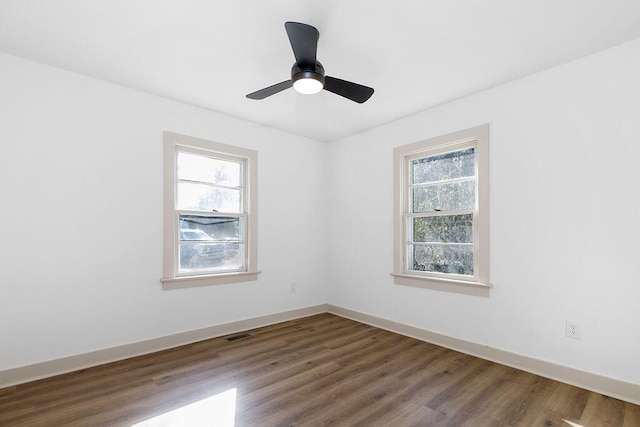 empty room featuring visible vents, dark wood-type flooring, a wealth of natural light, and baseboards