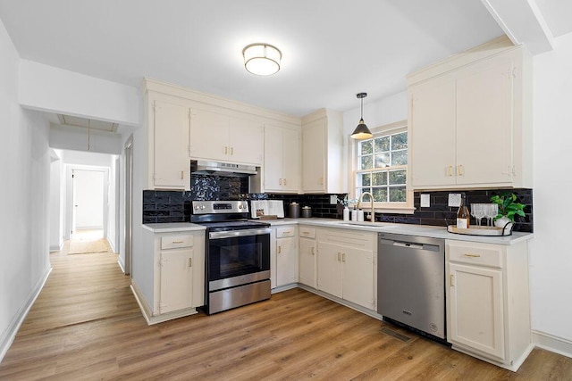 kitchen featuring under cabinet range hood, stainless steel appliances, a sink, light countertops, and light wood-type flooring