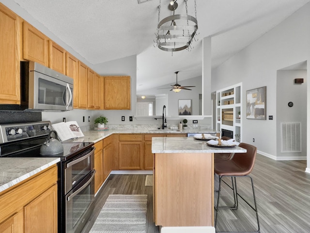 kitchen with lofted ceiling, stainless steel appliances, sink, dark hardwood / wood-style floors, and a breakfast bar area