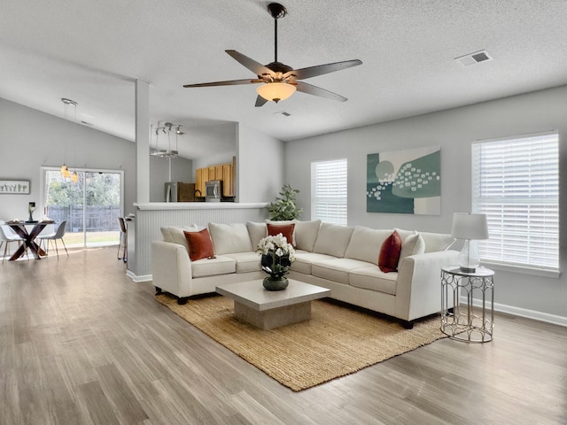 living room with lofted ceiling, light wood-type flooring, a textured ceiling, and ceiling fan