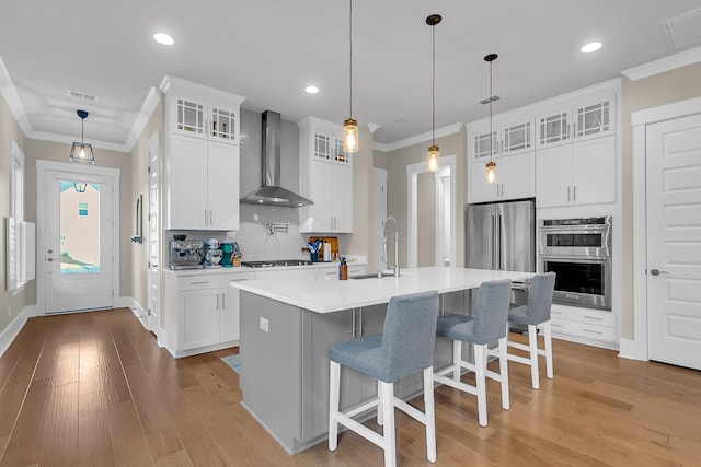 kitchen with wall chimney exhaust hood, white cabinetry, stainless steel appliances, and an island with sink