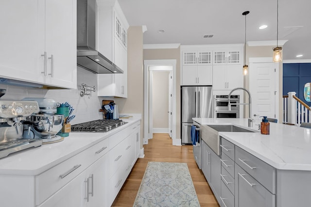 kitchen with wall chimney exhaust hood, a center island with sink, white cabinets, and hanging light fixtures