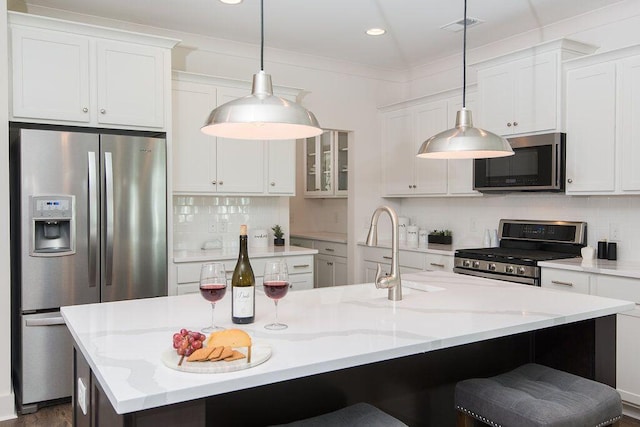 kitchen with white cabinetry, stainless steel appliances, a kitchen island with sink, and pendant lighting