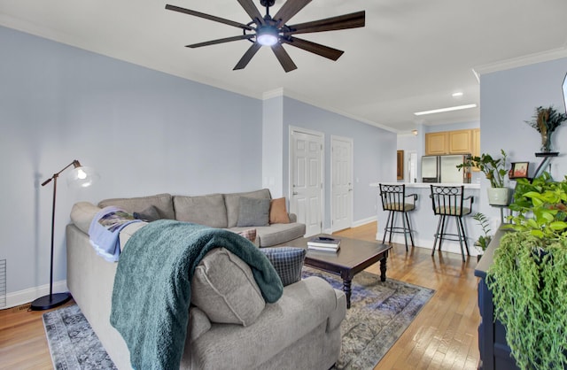 living room featuring ceiling fan, ornamental molding, and light wood-type flooring