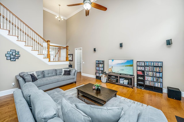 living room featuring hardwood / wood-style floors, ceiling fan with notable chandelier, crown molding, and a high ceiling