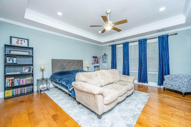 bedroom with hardwood / wood-style flooring, ceiling fan, crown molding, and a tray ceiling