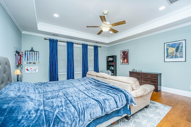 bedroom with wood-type flooring, a raised ceiling, ceiling fan, and crown molding