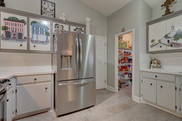 kitchen with light tile patterned flooring, appliances with stainless steel finishes, white cabinetry, lofted ceiling, and backsplash