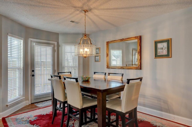 dining space with an inviting chandelier, wood-type flooring, and a textured ceiling