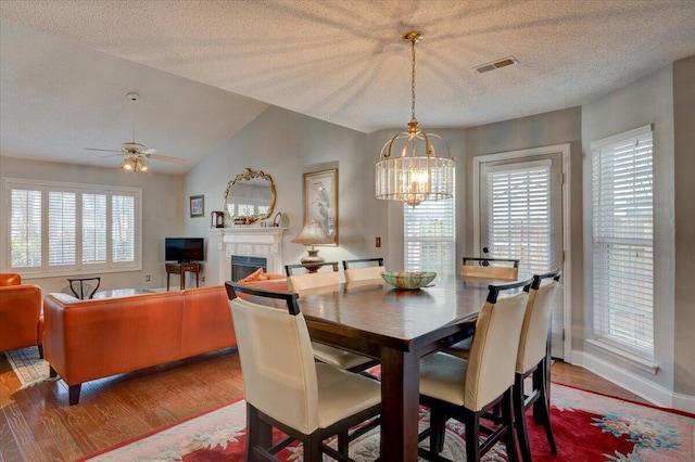 dining space featuring ceiling fan with notable chandelier, wood-type flooring, a textured ceiling, and vaulted ceiling