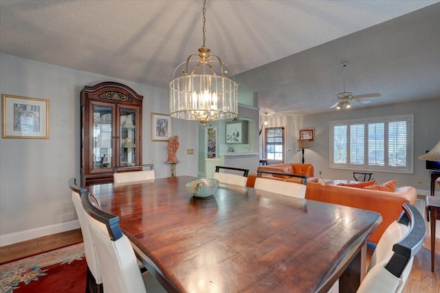 dining room with ceiling fan with notable chandelier, lofted ceiling, hardwood / wood-style floors, and a textured ceiling