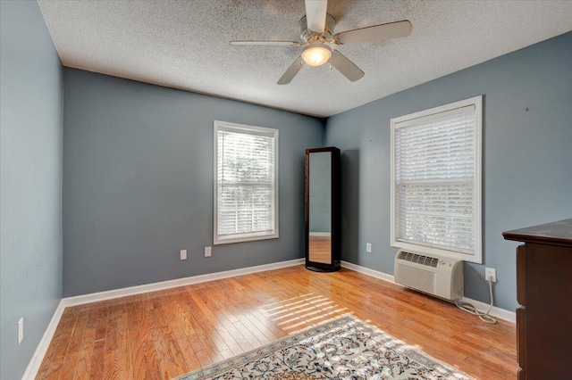 unfurnished living room featuring a wall mounted air conditioner, light hardwood / wood-style floors, a textured ceiling, and ceiling fan