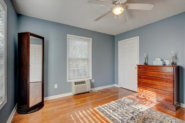 bedroom with ceiling fan, a wall mounted AC, light hardwood / wood-style flooring, and a textured ceiling