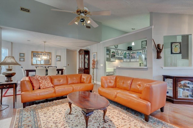 living room featuring vaulted ceiling, ceiling fan with notable chandelier, a textured ceiling, and light wood-type flooring