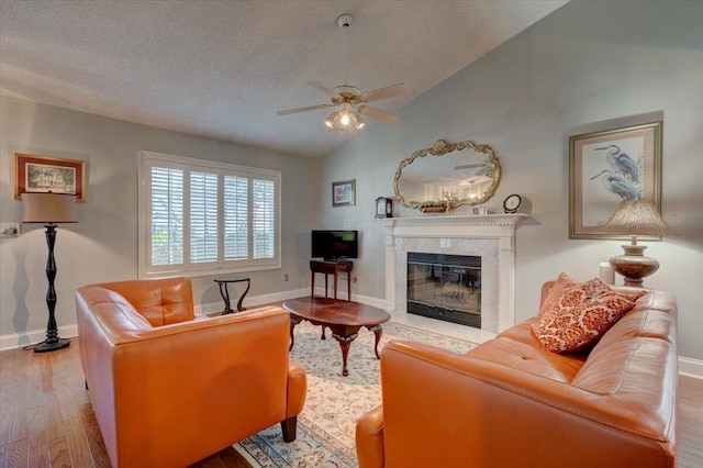 living room featuring light hardwood / wood-style flooring, a premium fireplace, ceiling fan, a textured ceiling, and vaulted ceiling