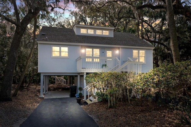 coastal inspired home with a carport, stairway, driveway, covered porch, and roof with shingles