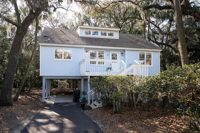 raised beach house featuring a carport, stairway, asphalt driveway, a porch, and roof with shingles