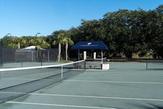 view of tennis court with fence and view of wooded area