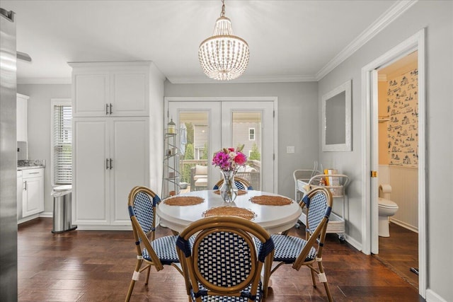 dining area with dark wood finished floors, a chandelier, ornamental molding, and a wainscoted wall