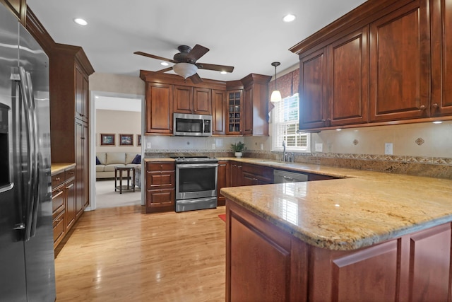 kitchen with kitchen peninsula, appliances with stainless steel finishes, ceiling fan, decorative light fixtures, and light hardwood / wood-style floors