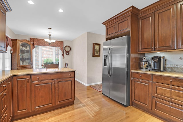 kitchen with light stone countertops, hanging light fixtures, stainless steel refrigerator with ice dispenser, a chandelier, and light hardwood / wood-style floors