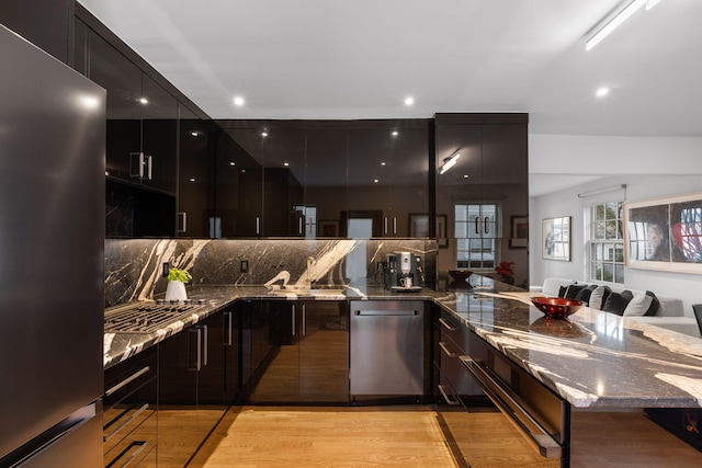 kitchen with stainless steel appliances, sink, dark stone countertops, light hardwood / wood-style floors, and tasteful backsplash