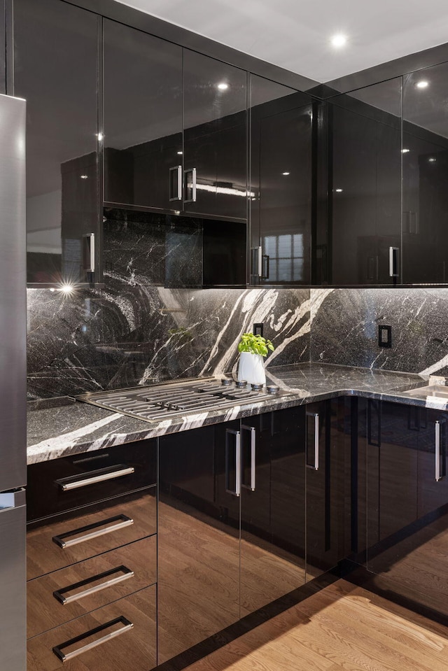 bar with decorative backsplash, dark stone countertops, light hardwood / wood-style floors, and stainless steel fridge