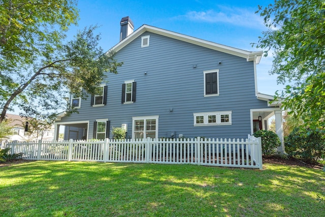 back of house with a fenced front yard, a chimney, and a lawn