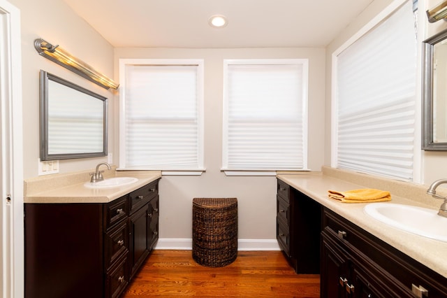 bathroom featuring wood finished floors, two vanities, a sink, and baseboards