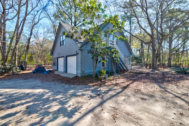 view of home's exterior with a garage, a shingled roof, fence, stairs, and dirt driveway